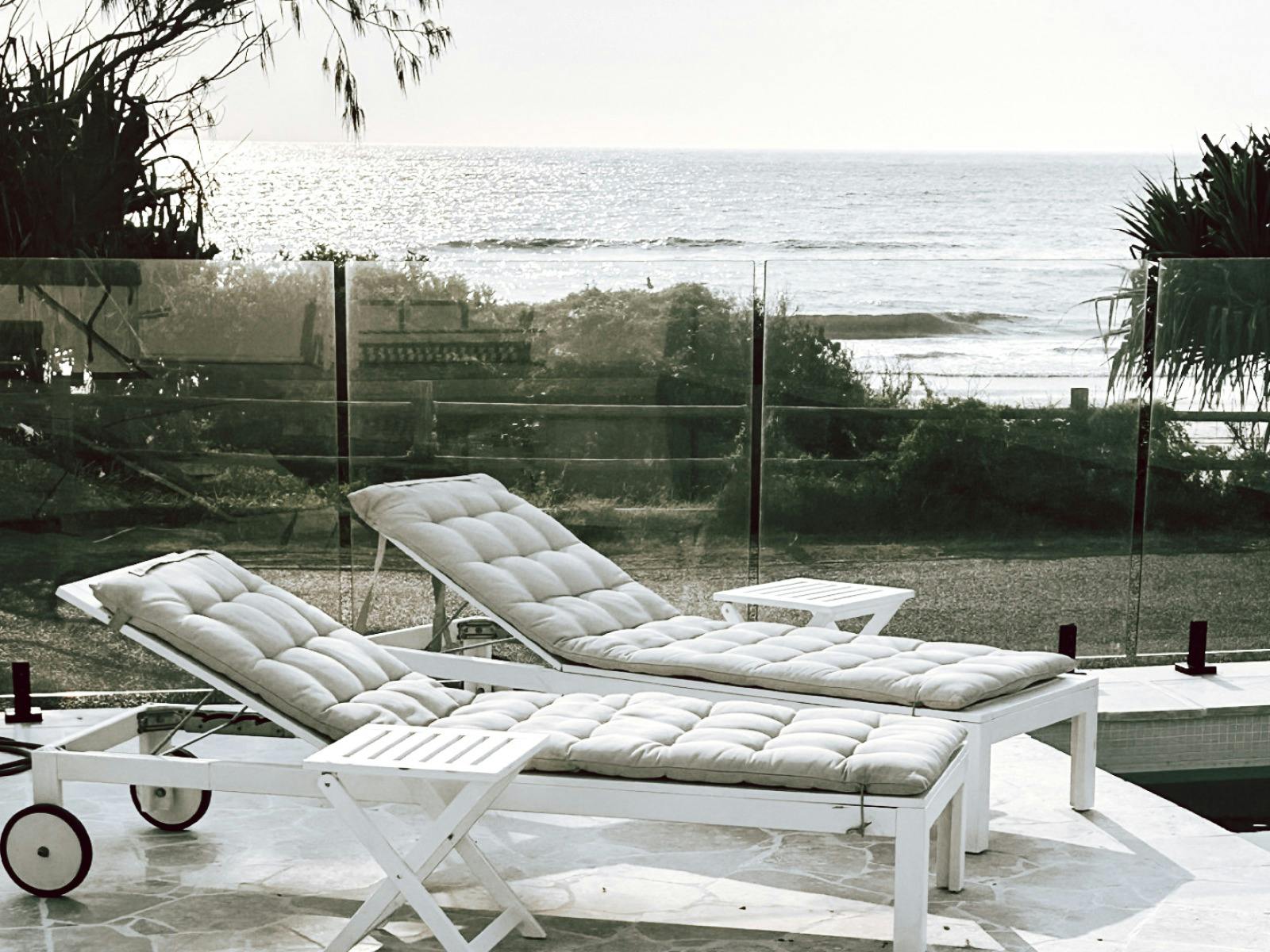 Lounge deck chairs with cushions in front of glass balustrade with ocean view