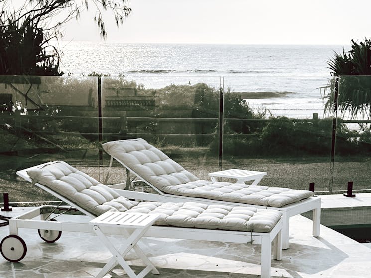 Lounge deck chairs with cushions in front of glass balustrade with ocean view