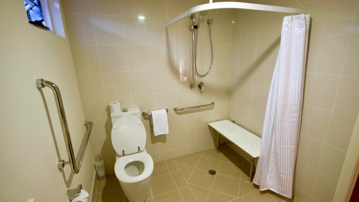 Accessible bathroom with grab rails, roll-in shower, fold-down shower seat and raised toilet at Doma