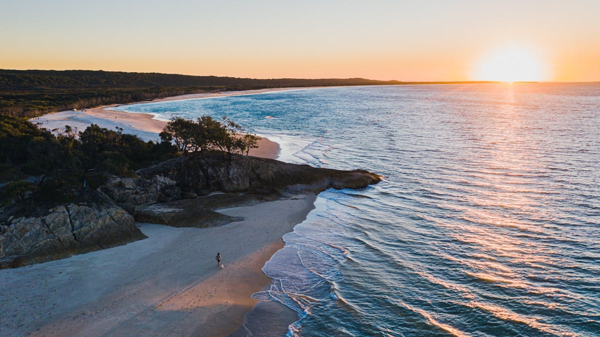 Aerial view of person walking dog on North Stradbroke Island beach at sunset