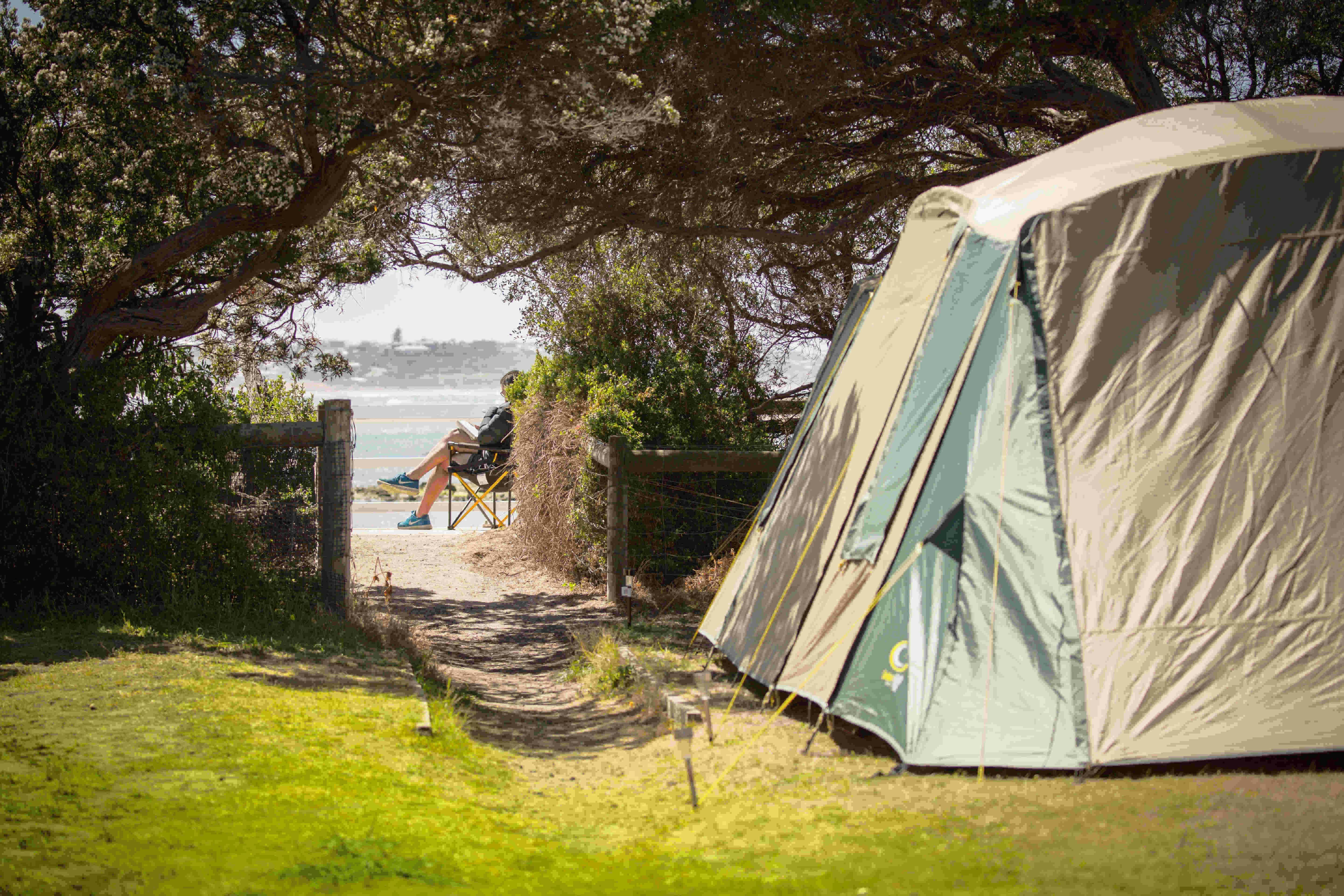 Man relaxing with a book beside his campsite on the Barwon Heads waterfront