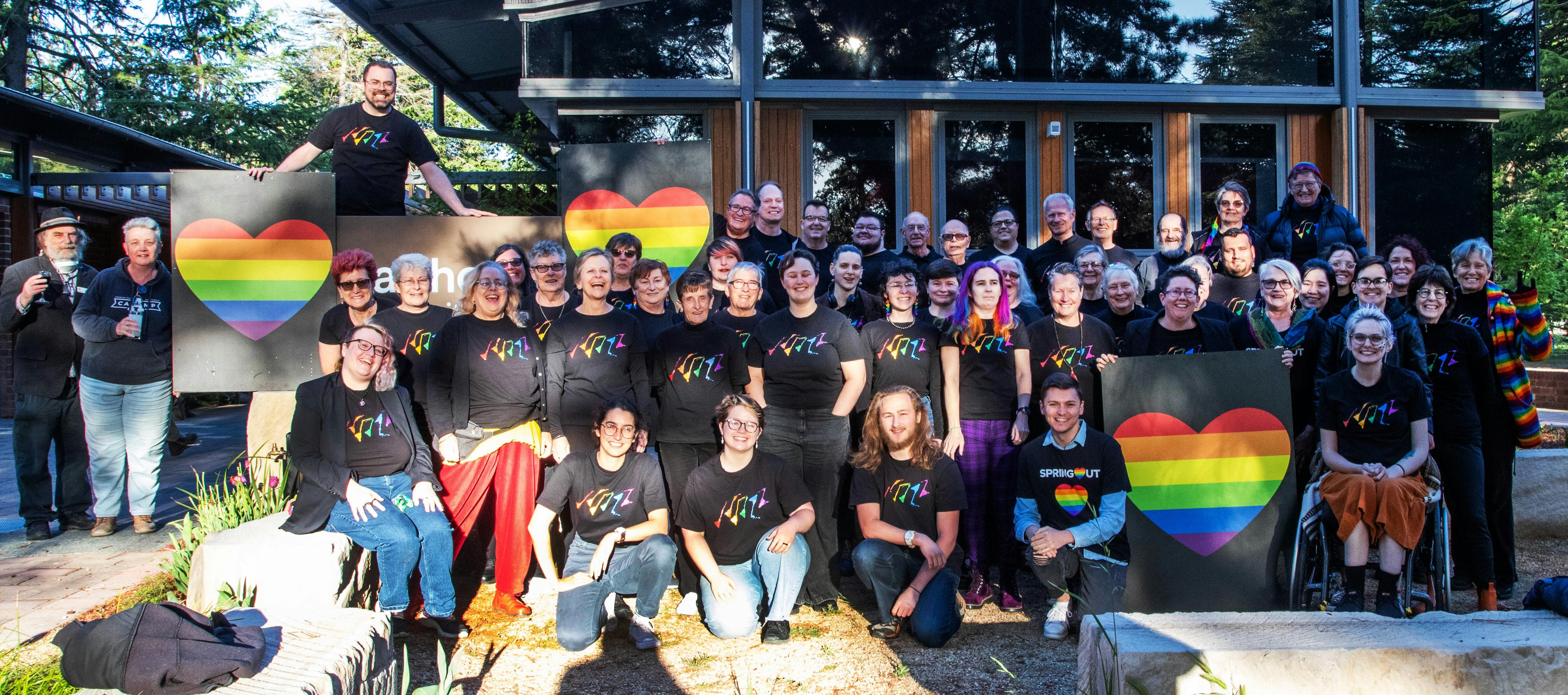 Picture of Canberra QWIRE people smiling and holding rainbow heart banners