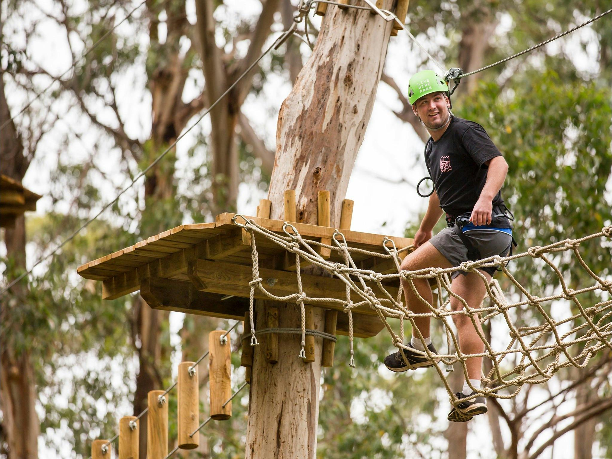 Man wearing a green helmet standing on a rope bridge