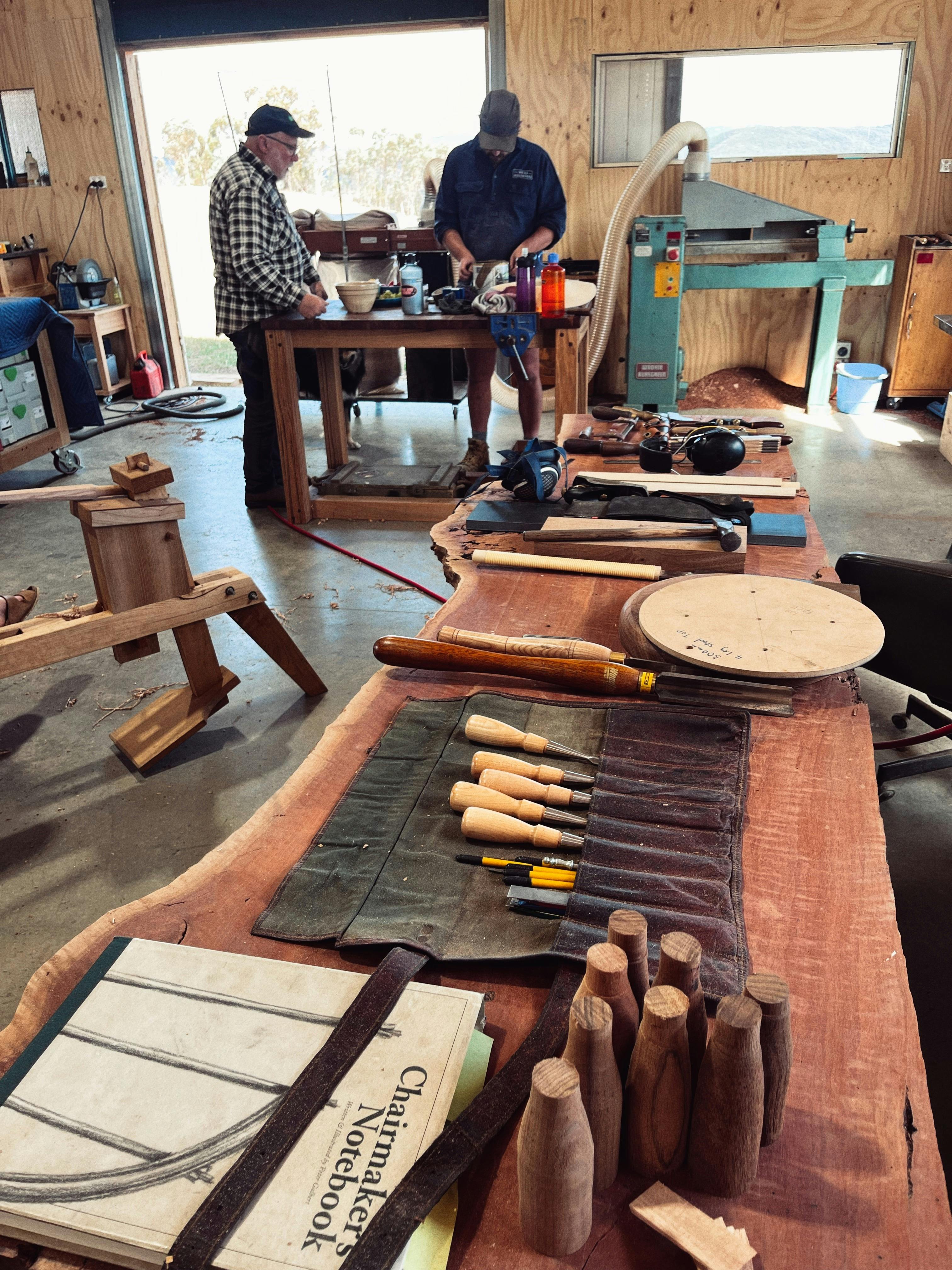 Chisels and handtools in the foreground and people making stools in the background