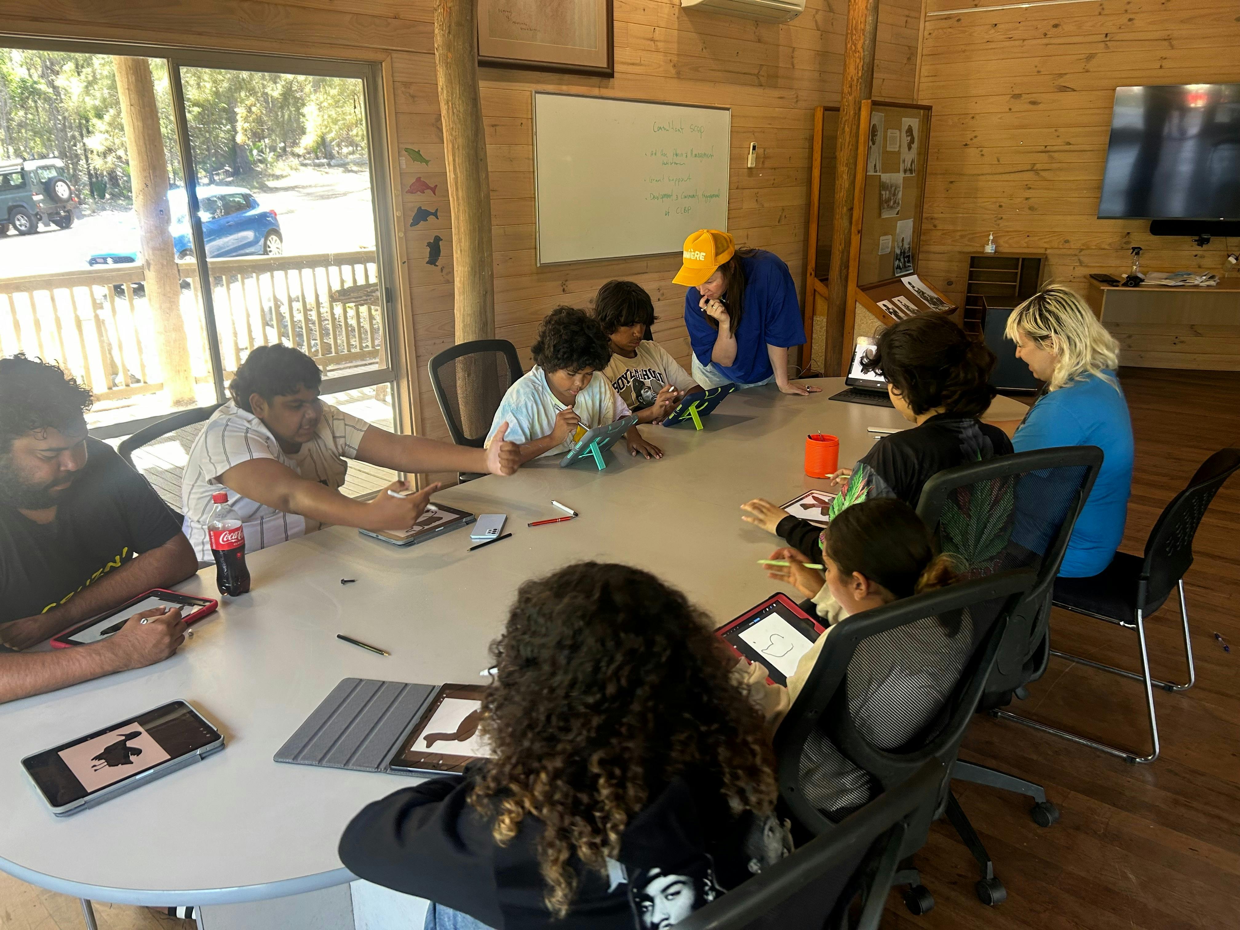 Young people sitting drawing on iPads whilst around an oval table
