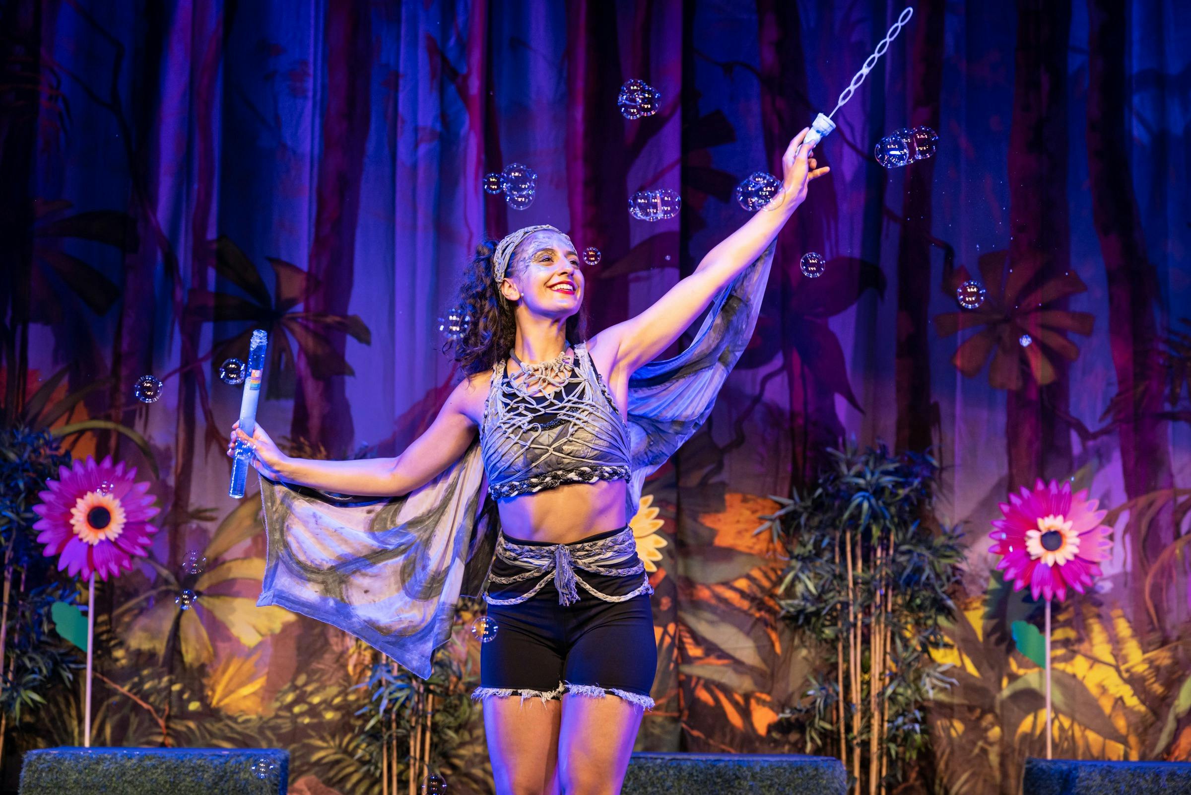One fairy stands on stage blowing bubbles