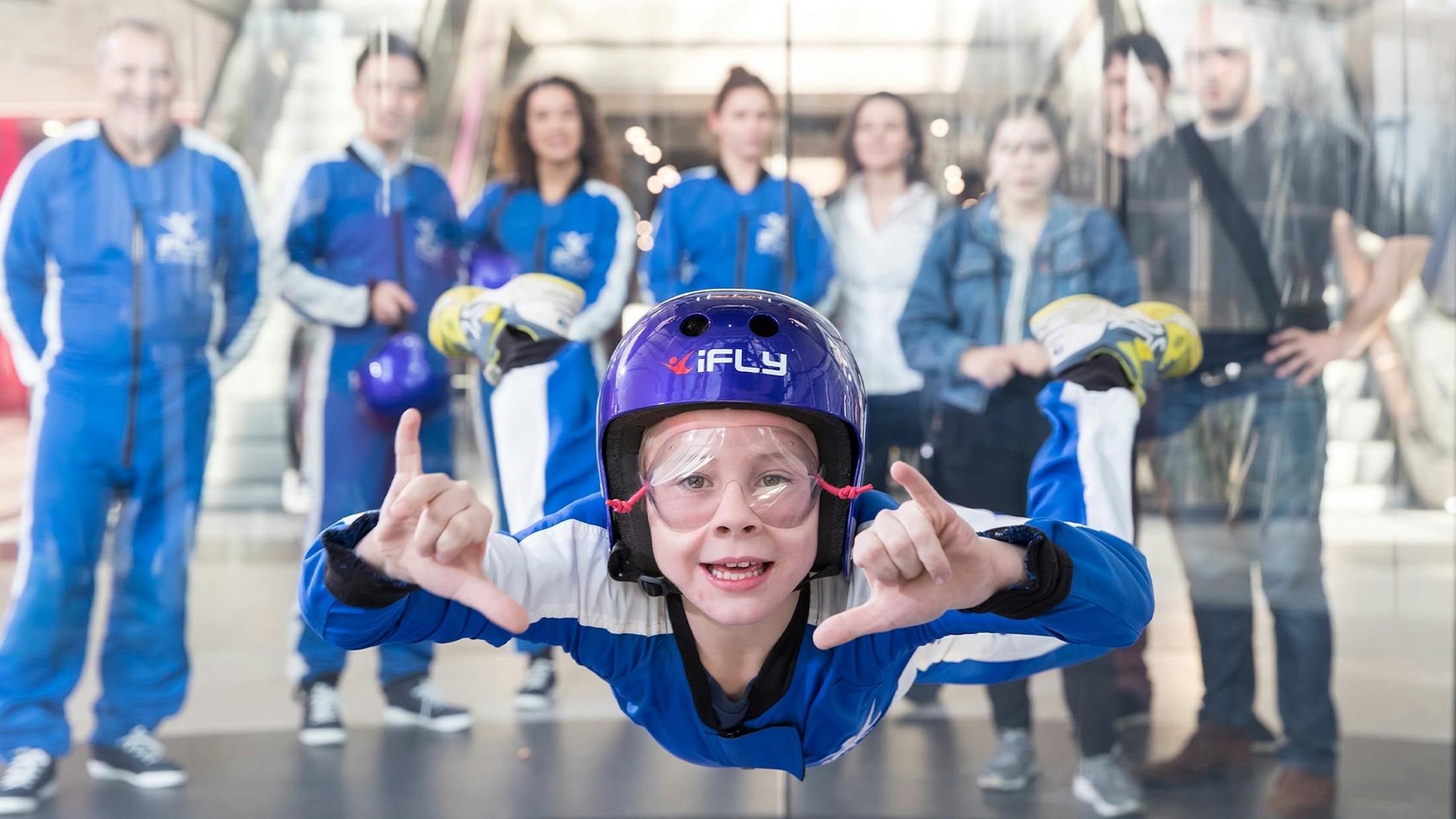Child smiles mid-flight as friends and family watch from behind the tunnel glass.