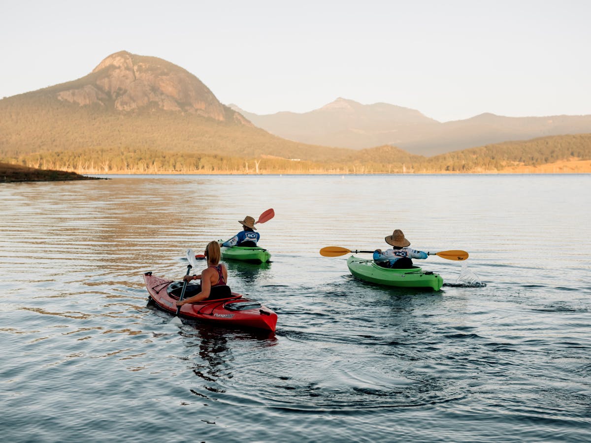 Three kayakers paddle across Lake Moogerah, with a range of mountains in the distance