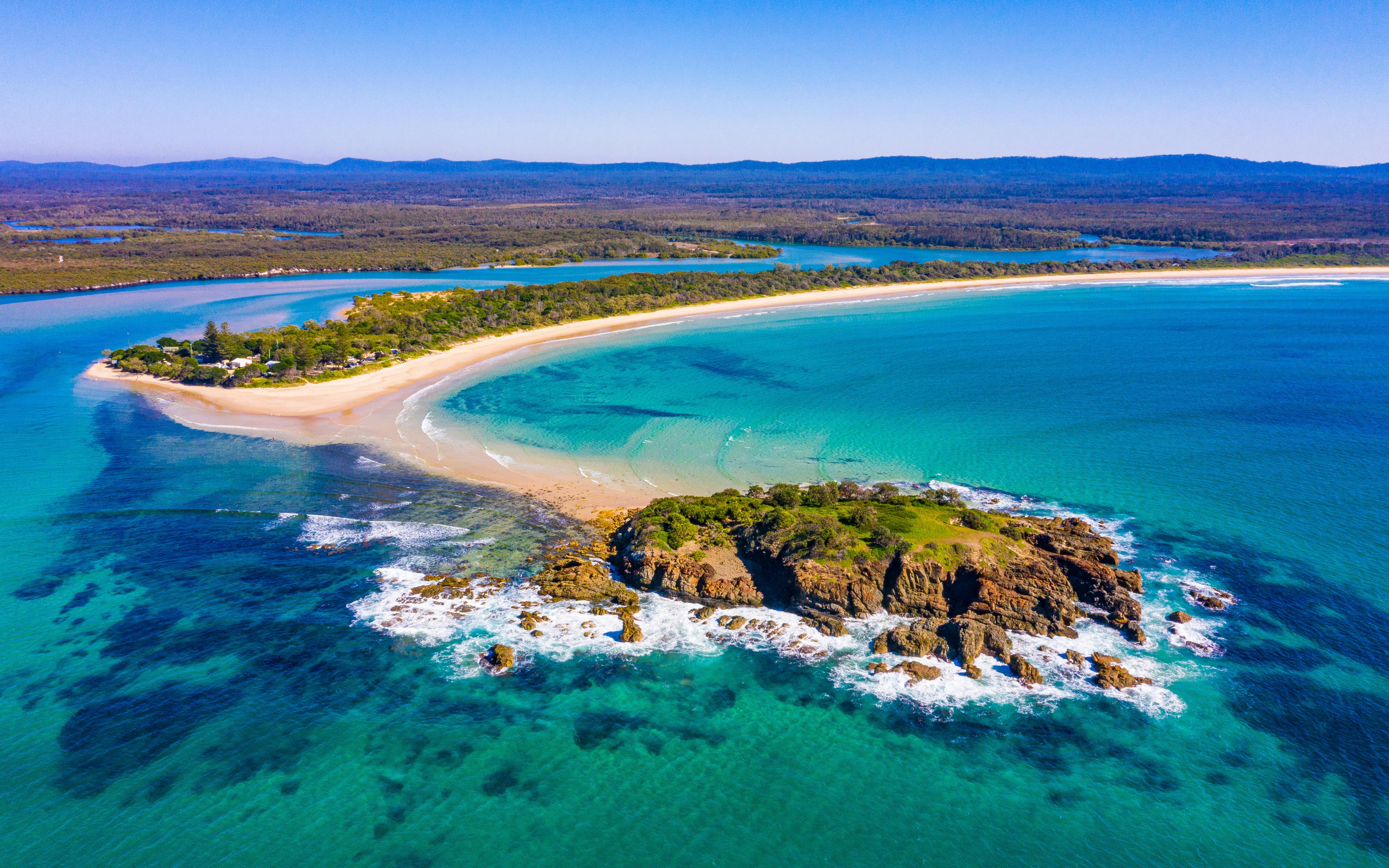 Ariel view of thin line of beach and a rocky outgroup surrounded by blue ocean