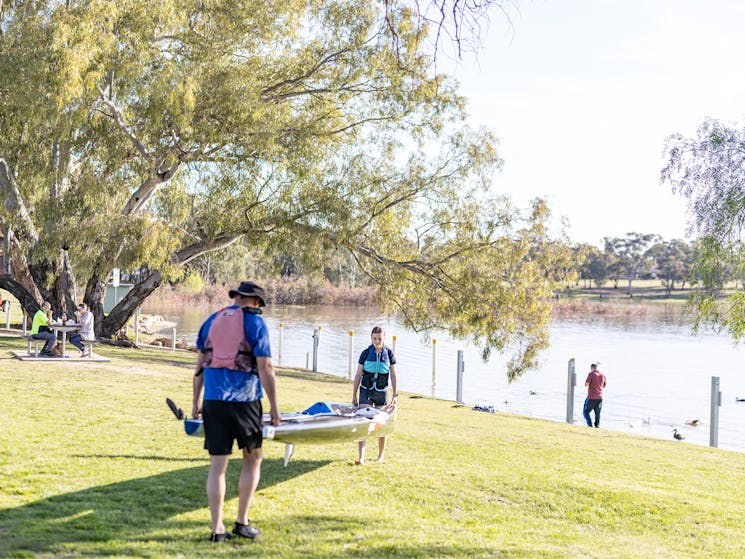 Two people lifting a kayak and walking towards the shores of Lake Albert