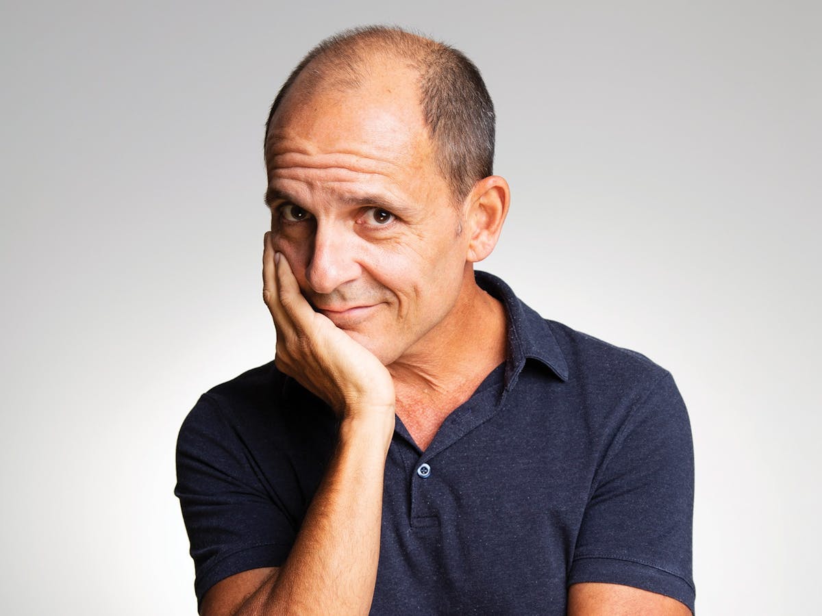 Comedian Carl Barron holding chin in hand starring straight ahead
