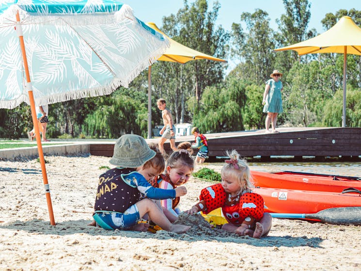 4 toddlers playing in the sand under a beach umbrella