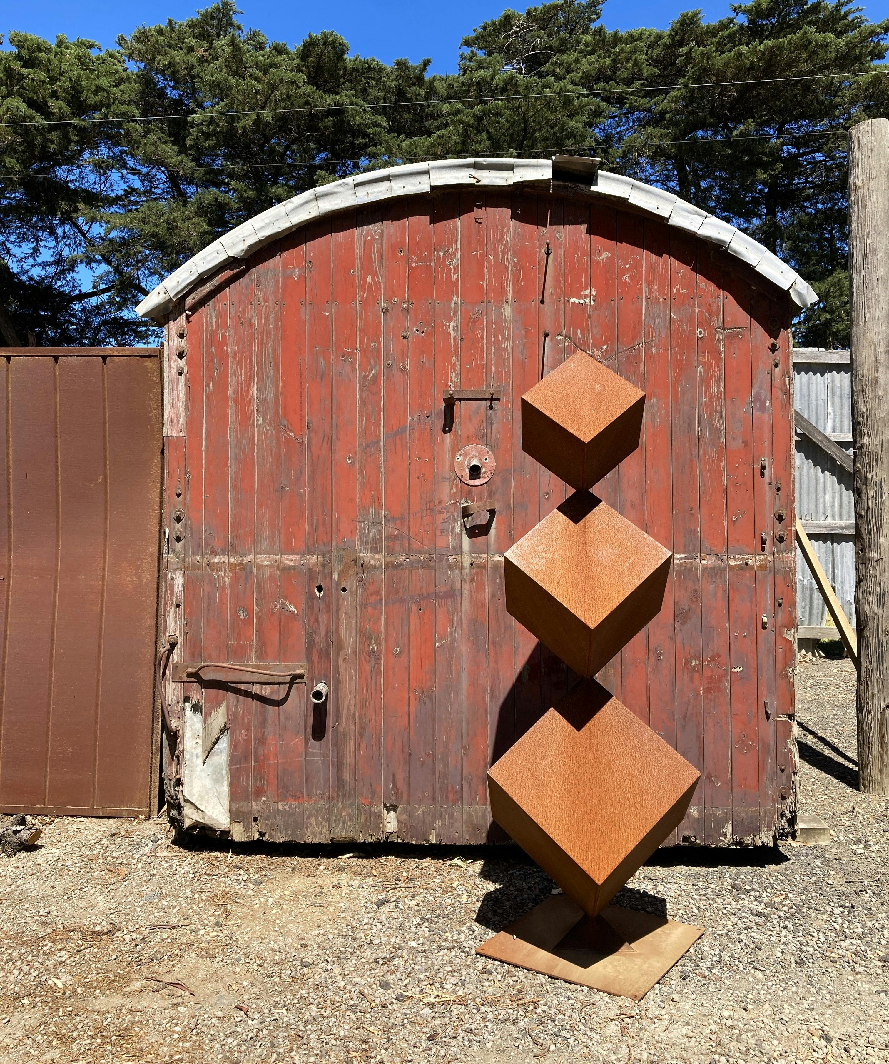 3 tiered corten steel sculpture pictured in front of a vintage train caboose