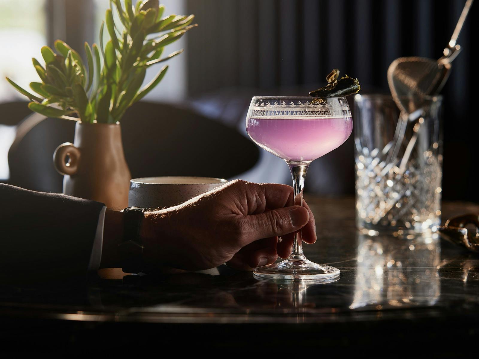A purple cocktail held in a masculine hand.