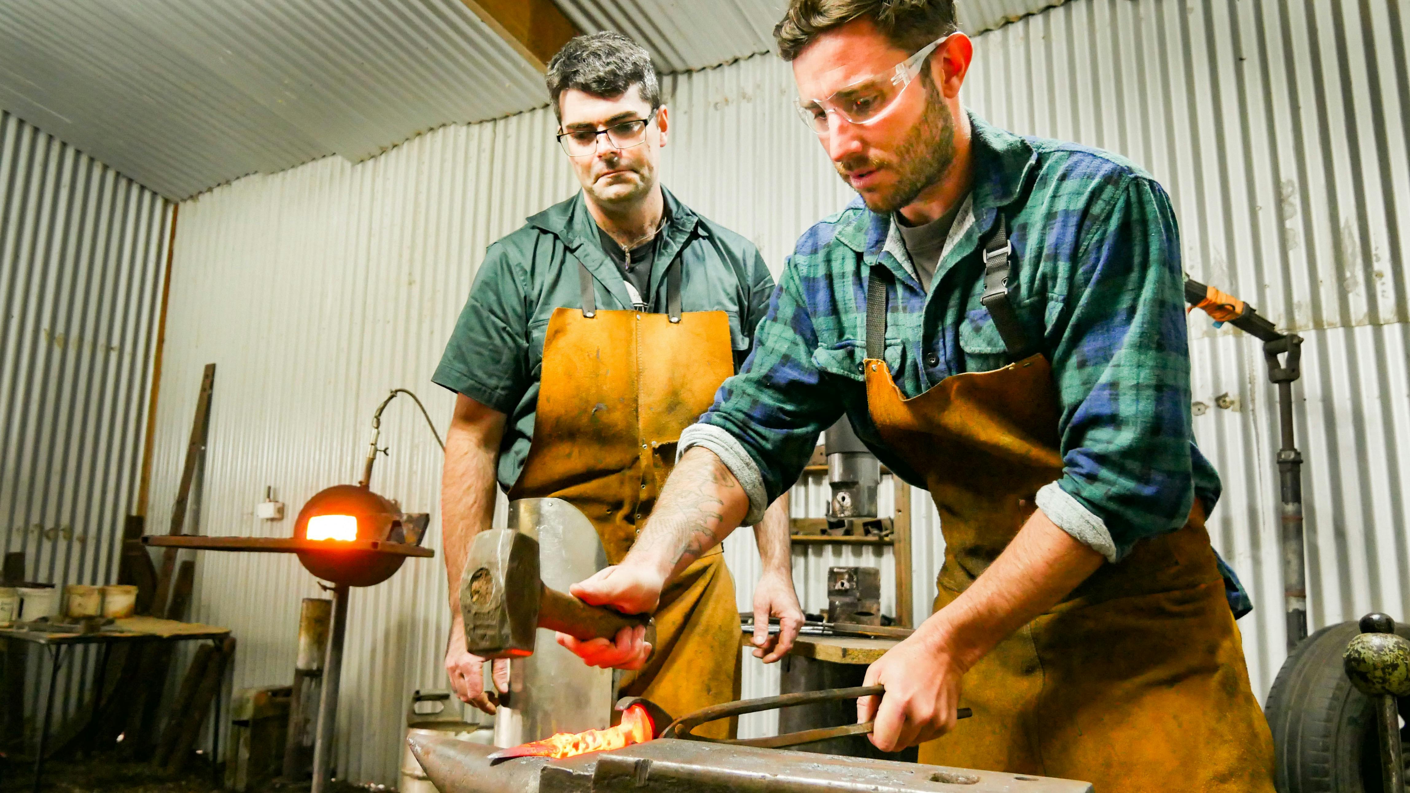 Tom overseeing a participant hitting a hot meal bottle opener on a traditional blacksmith anvil
