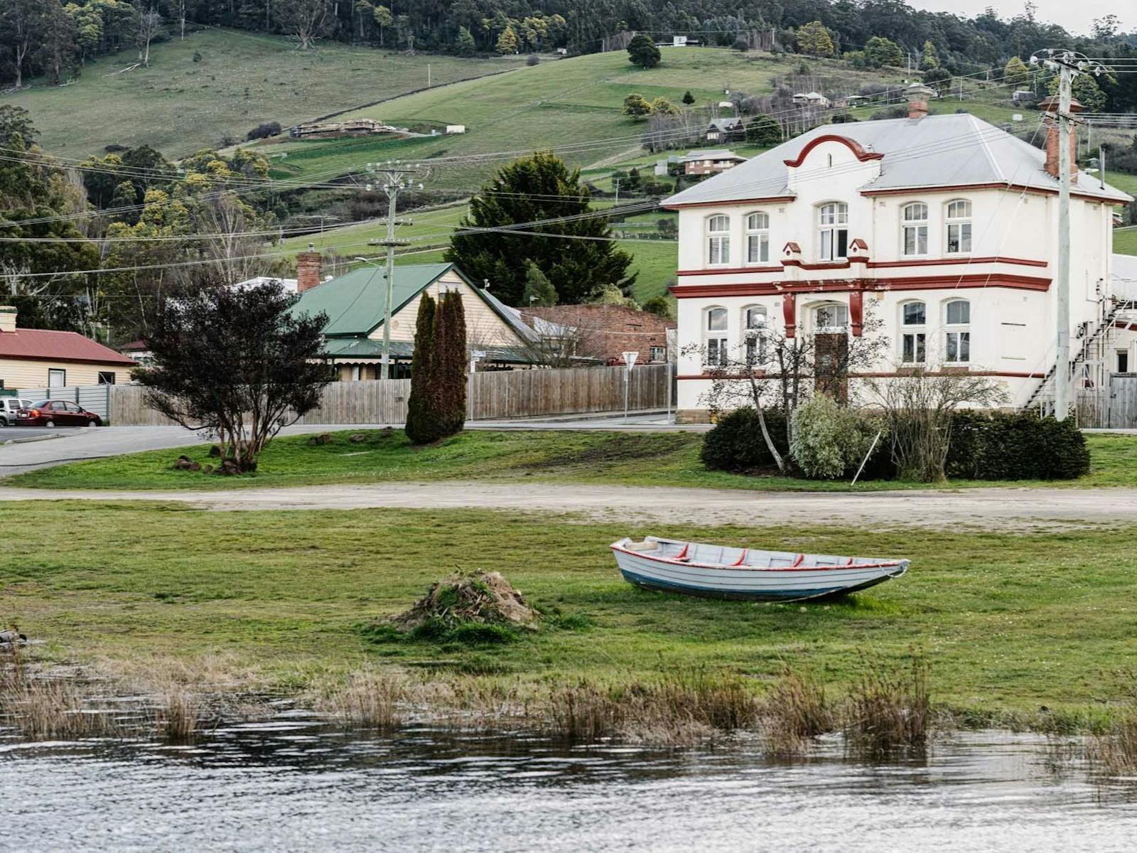 Two story Edwardian building on the banks of the Huon river , a row boat sits on the riverbank