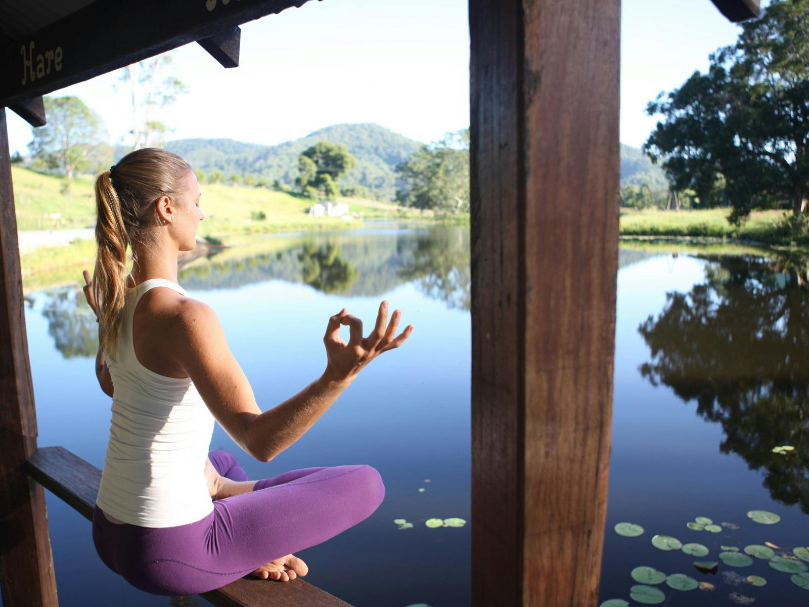A young woman meditating while overlooking a calm lake