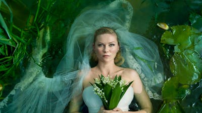 Woman with a blank expression lying down in white wedding gown and veil holding flowers