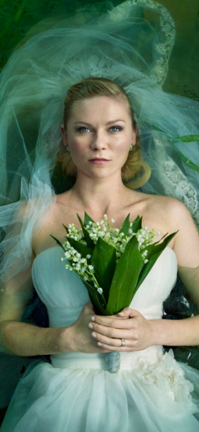 Woman with a blank expression lying down in white wedding gown and veil holding flowers