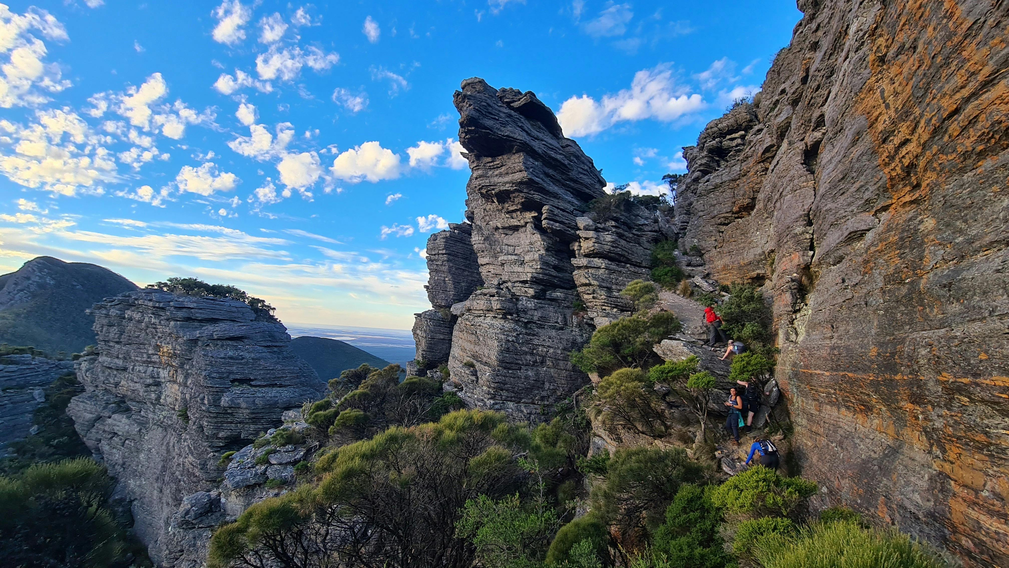 Rocky landscape, distant view of hikers climbing mountains along cliff edge to reach top of mountain