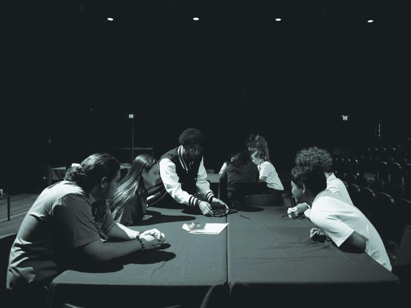 Photograph of students sitting at a table in the performance studio attending a music workshop.