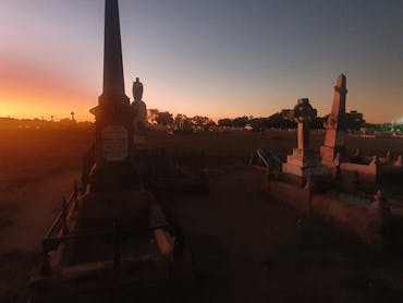Charters Towers Cemetery with a few grave statues and thesun setting in distance Charters Towers Cemetery with a few grave statues and thesun setting in distance