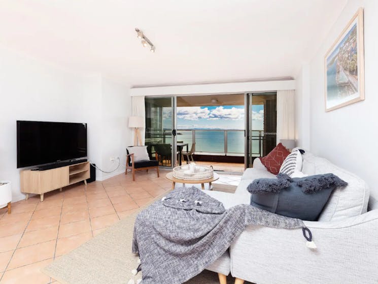 Loungeroom with spacious lounges, TV, out to balcony with 4 seater setting and stunning beach views