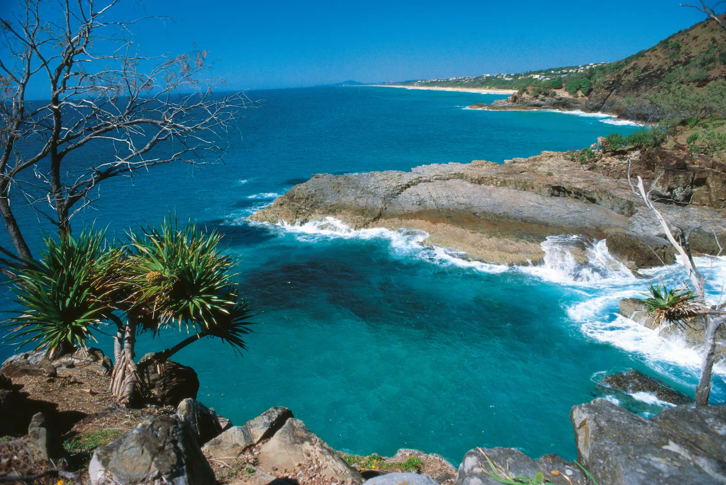 View over ocean and rocky promontory under blue sky.