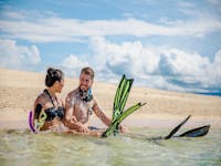 Young couple putting on their snorkel gear and smiling by the beach