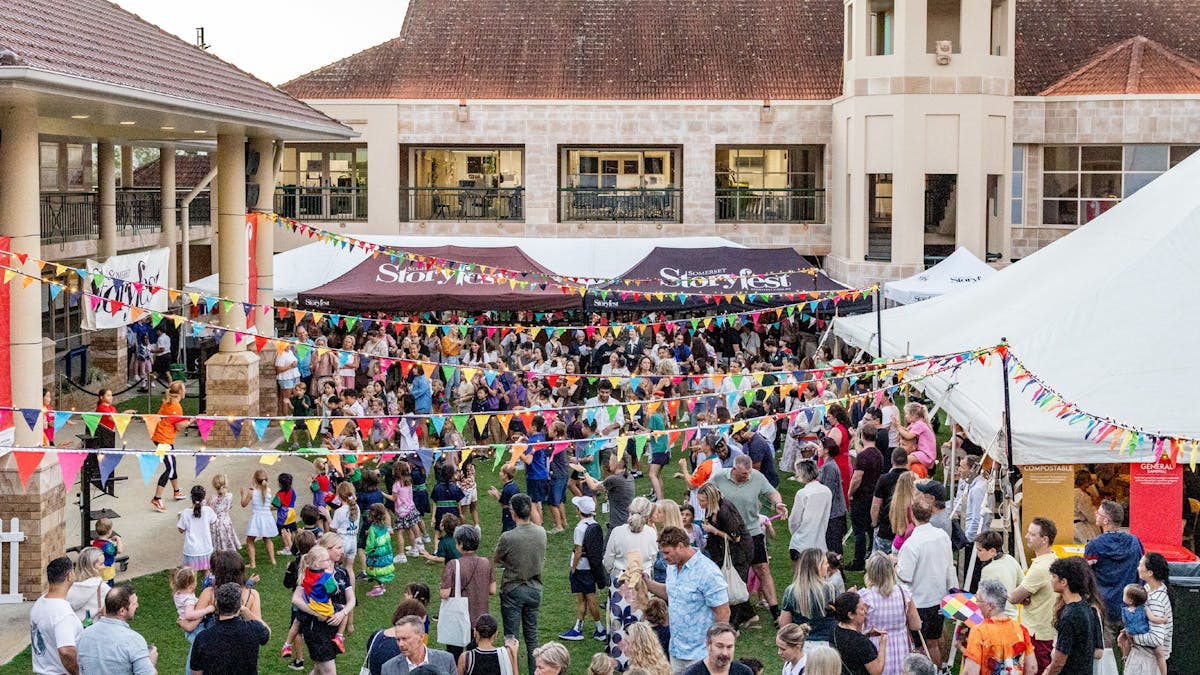 Families and children enjoying a busy outdoor festival courtyard decorated with colourful bunting.