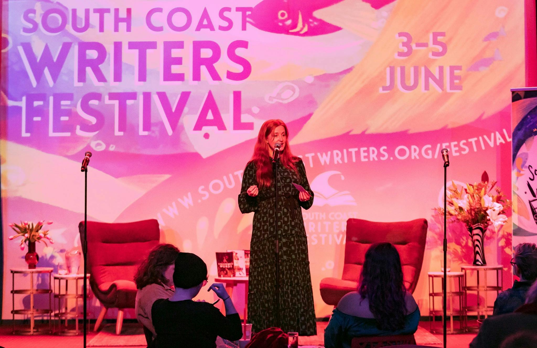 Director Sarah Nicholson standing on stage speaking into a microphone