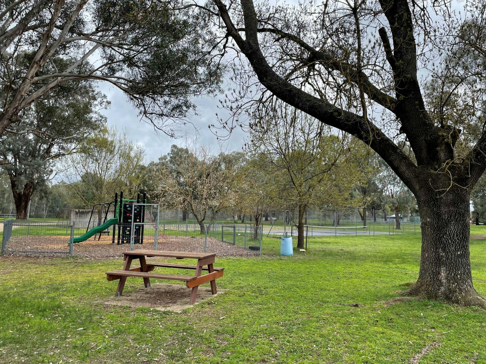 Small fenced playground beind a picnic table on green grass