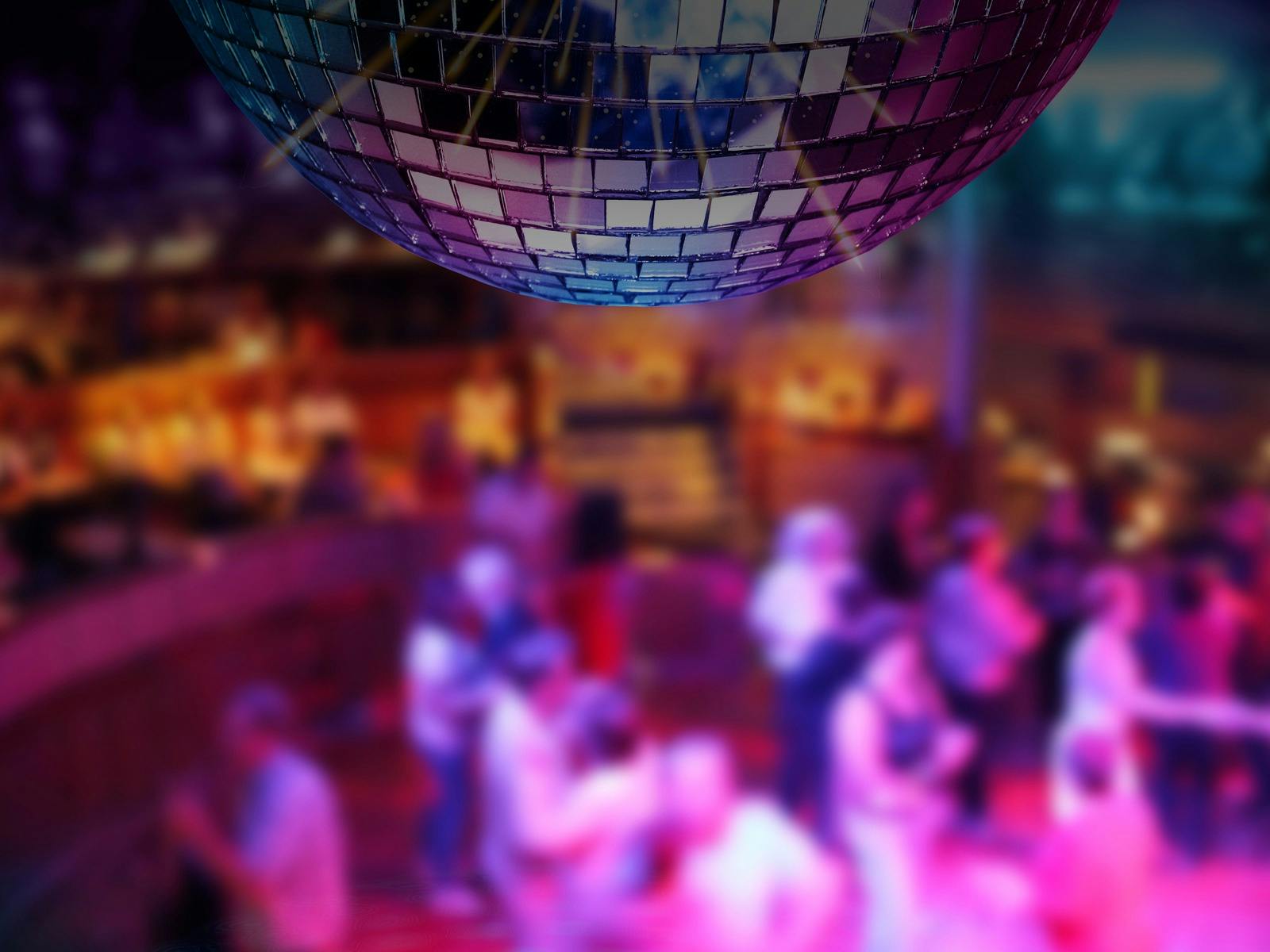 Older adults dancing at a New Year's Eve party with a disco ball and fireworks, family-friendly.