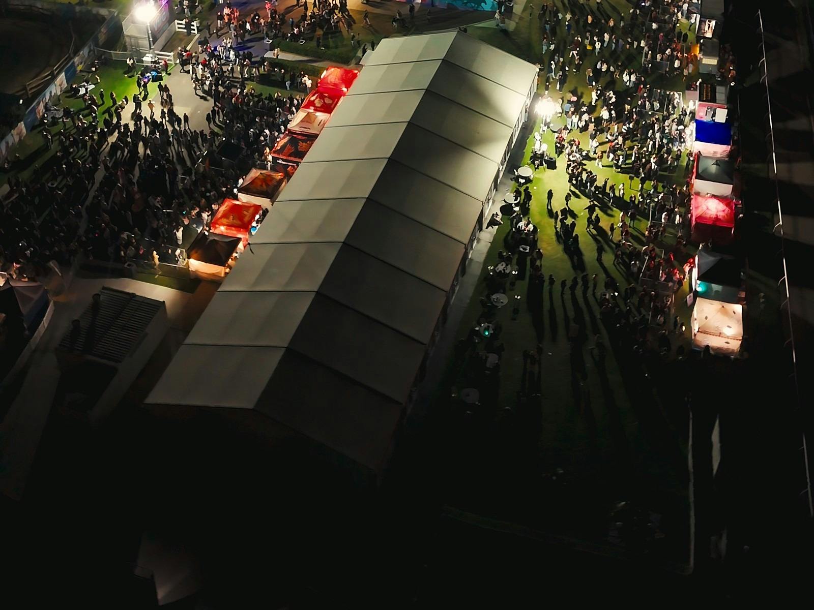 Night aerial view of crowds walking between food stalls and a marquee