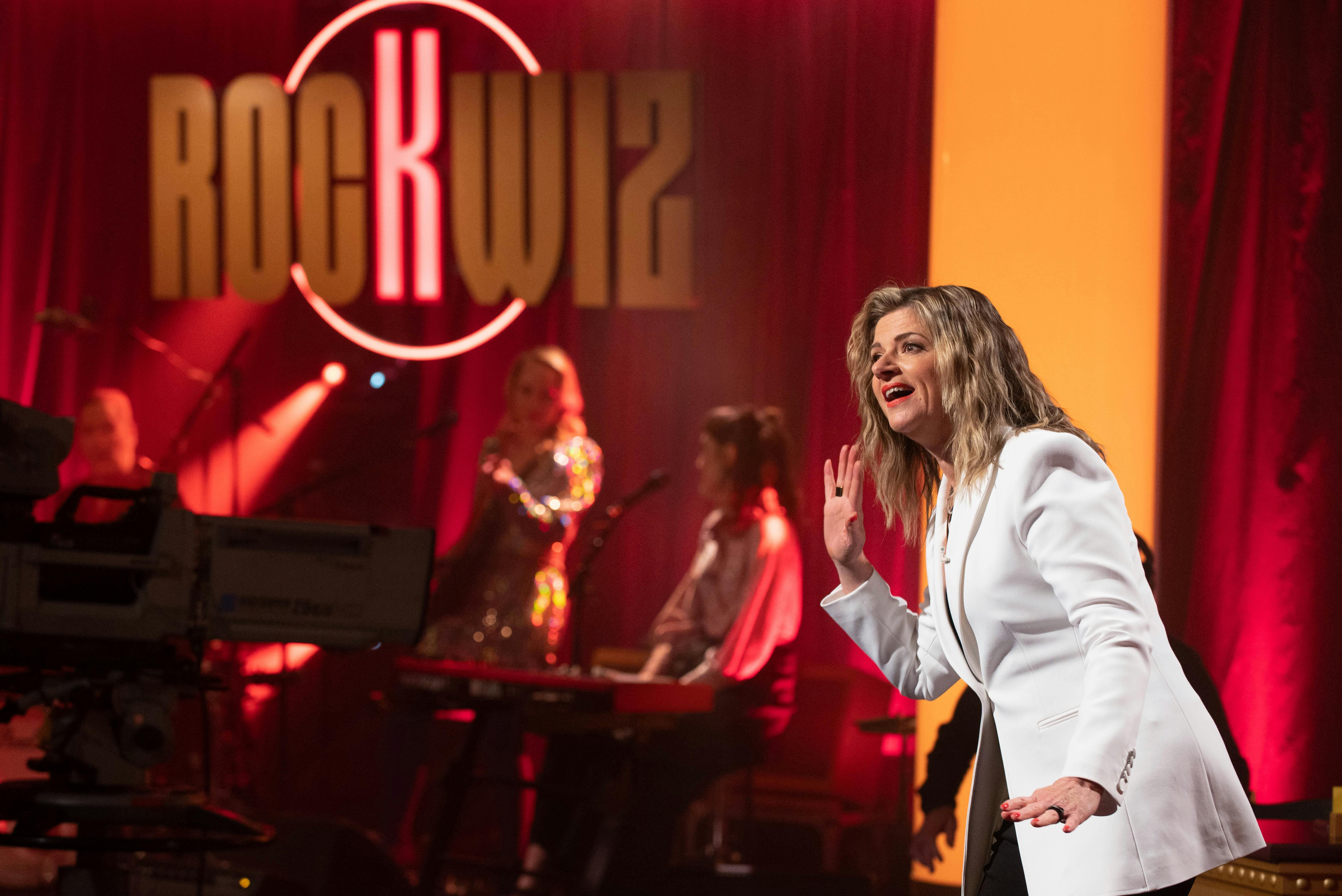 A women in a white blazer leaning towards an audience