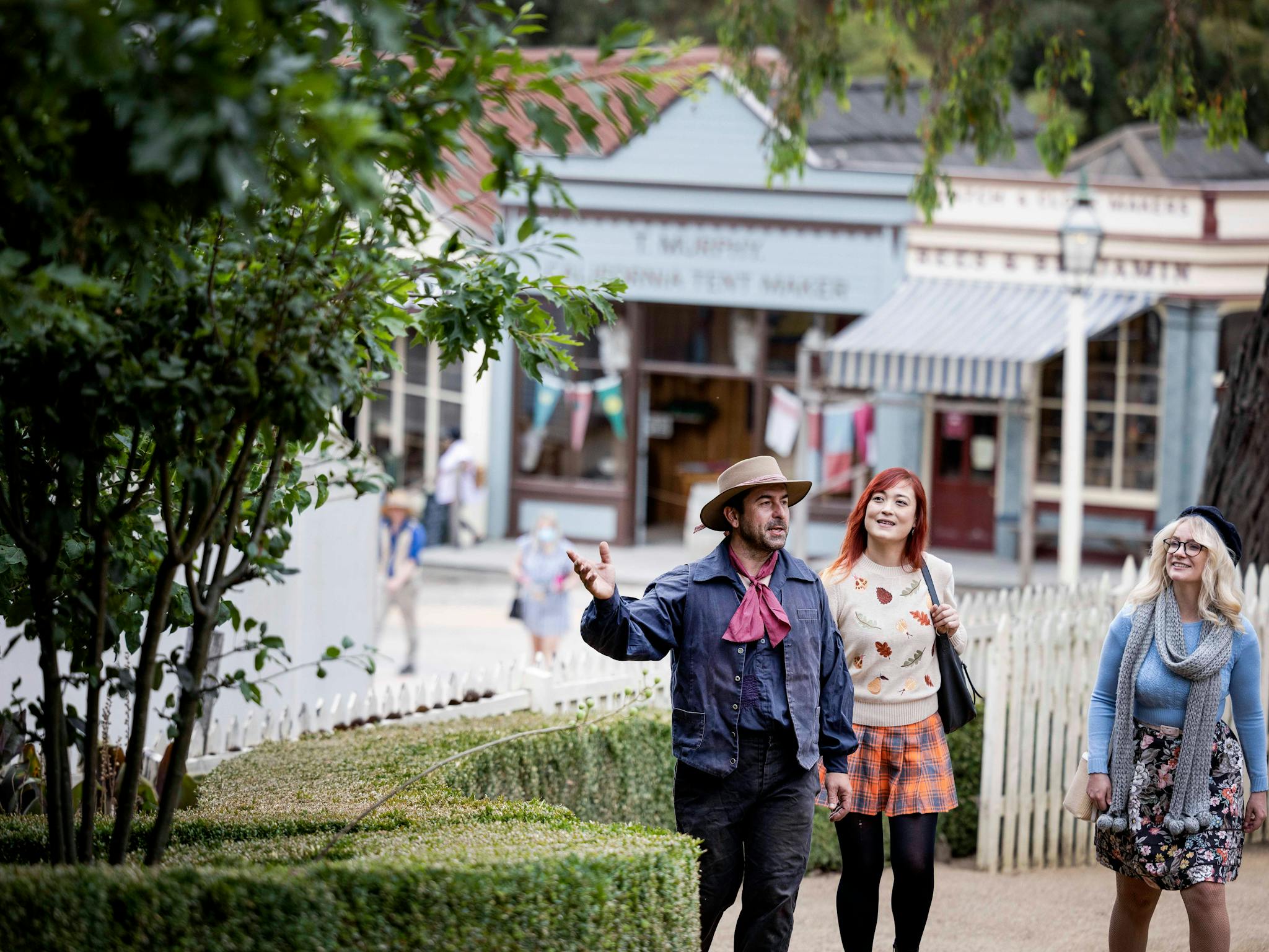 Two women walking through Sovereign Hill gardens with costumed guide