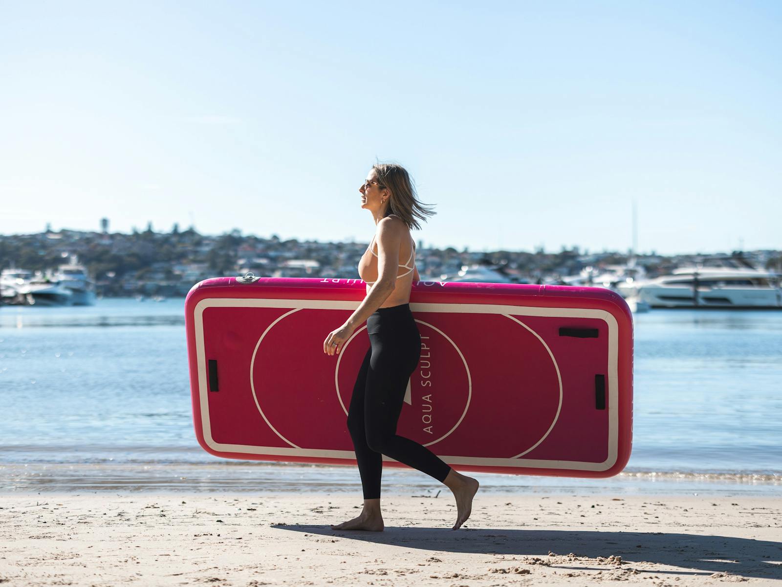 Founder Nina Hirschfeld walking along Bellamy beach in Rose Bay Sydney holding an Aqua Sculpt board