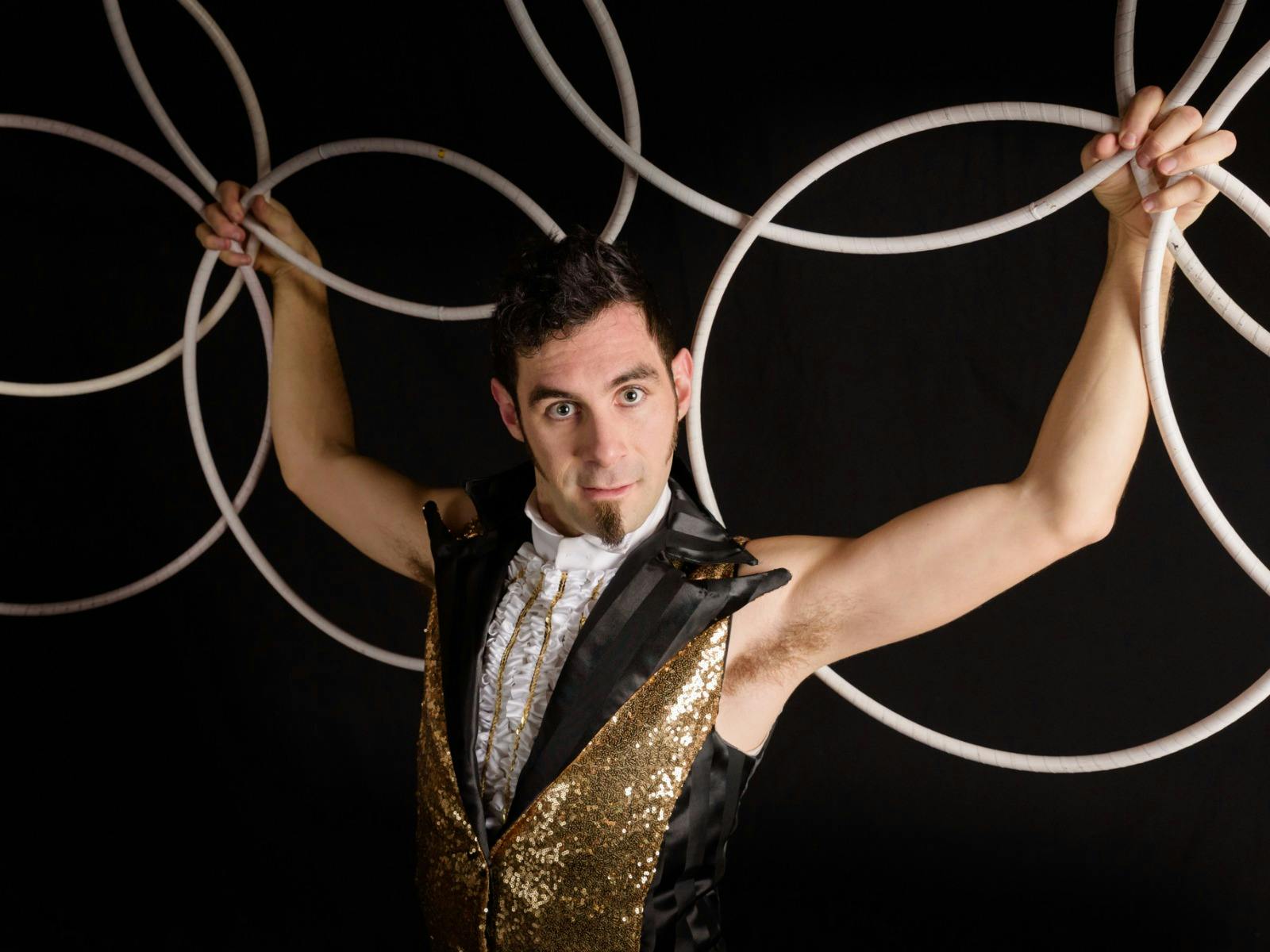 A man in a golden vest holds multiple silver metal hoops in a pattern while looking at the camera