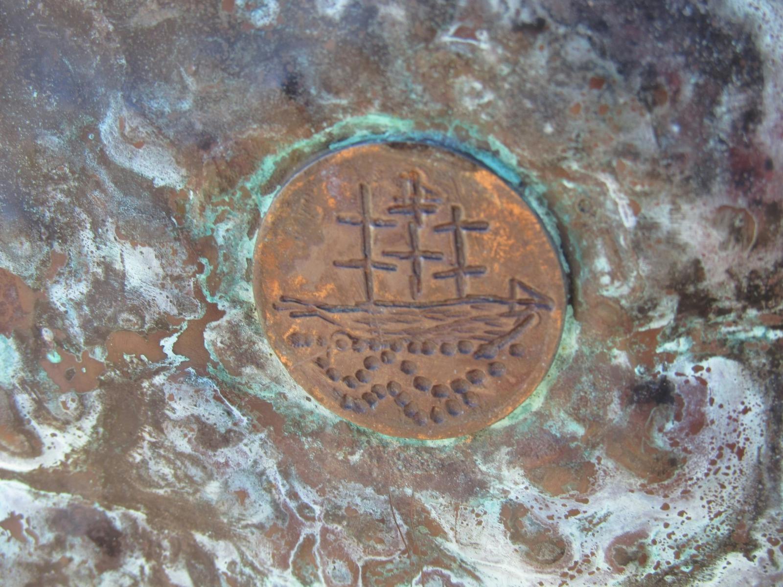 This close up of a copper disc has an engraving of a three masted sailing ship