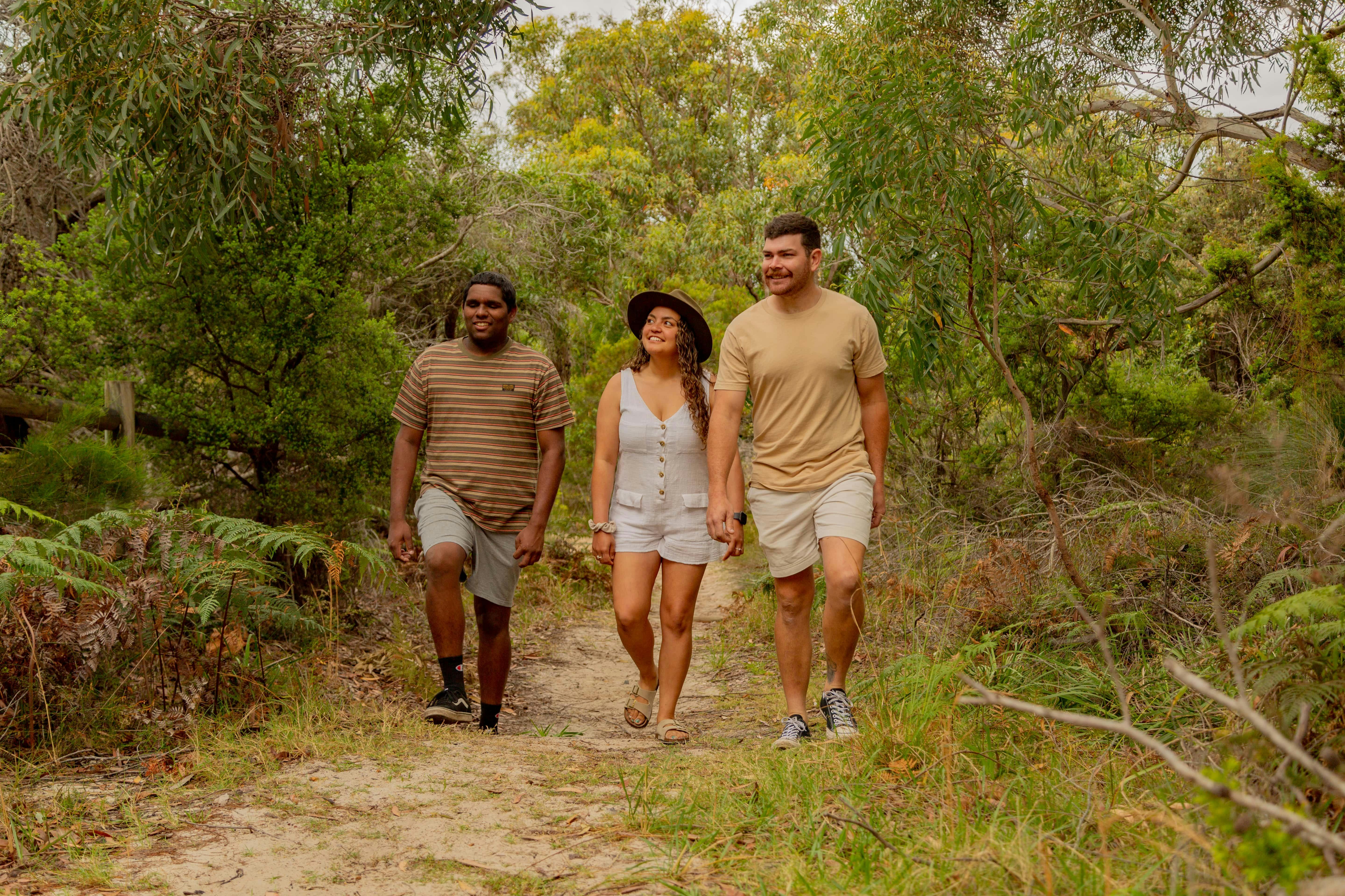 Two men and a lady walking through the bush on a path.