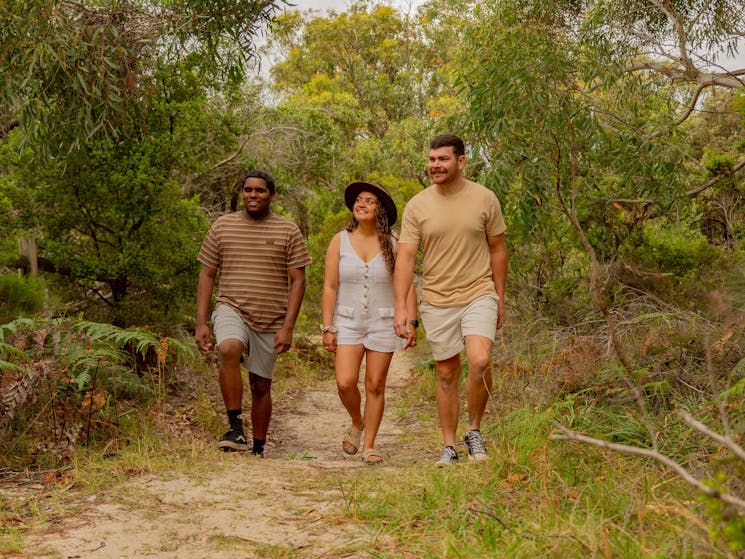 Two men and a lady walking through the bush on a path.