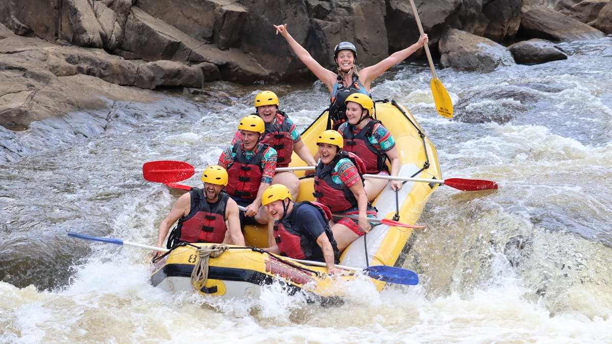 Group of 6 smiling at the camera in the middle of a rapid as their guide lifts both arms victorious