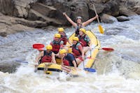 Group of 6 smiling at the camera in the middle of a rapid as their guide lifts both arms victorious