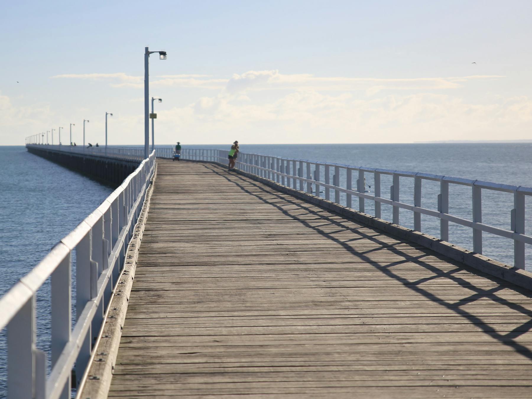photo showing the wooden walkway on Urangan Pier stretching into the distance with people fishing