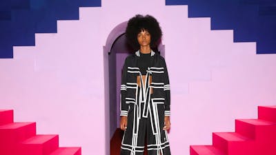 Lady modelling outfit behind pink stairs and purple background