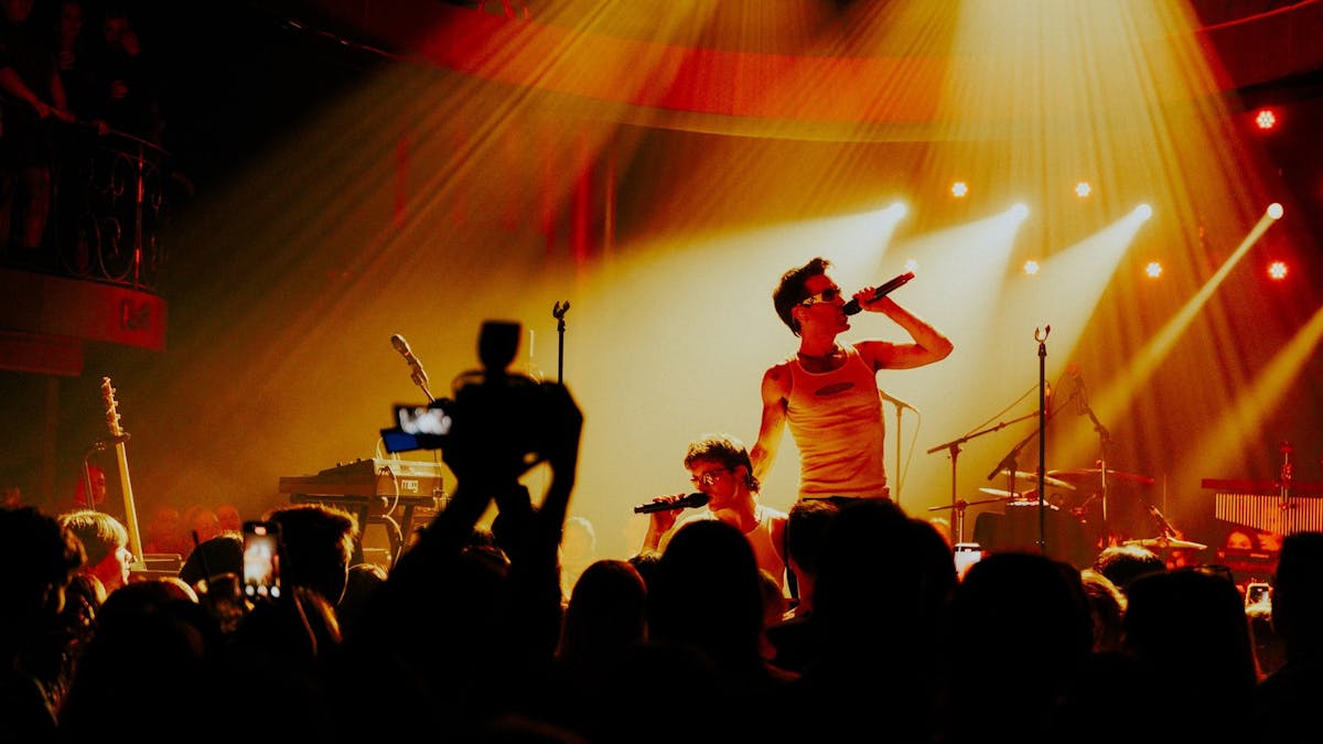 A musician in a white shirt s silhouetted against stage lights in front a big crowd