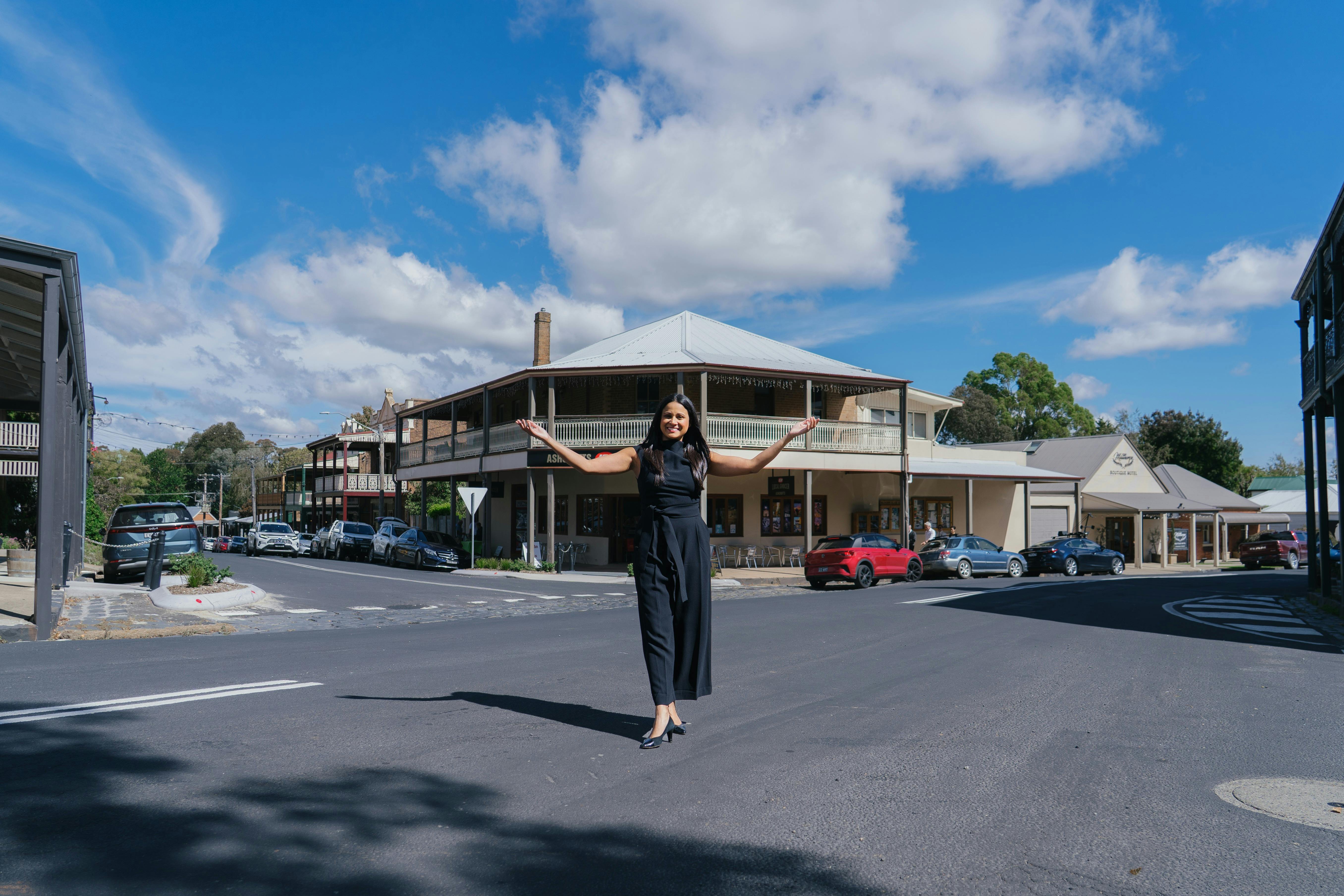 A female singer stands in the streets of Millthorpe with her arms out welcoming and smiling