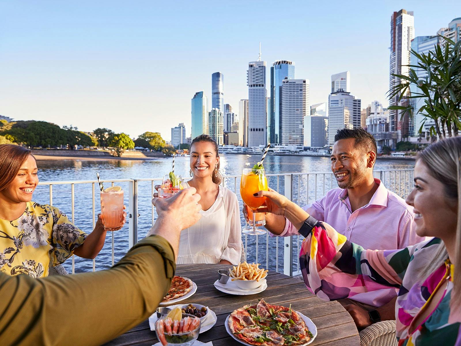A group of friends alfresco dining and cheering over cocktails at riverside bar brisbane city