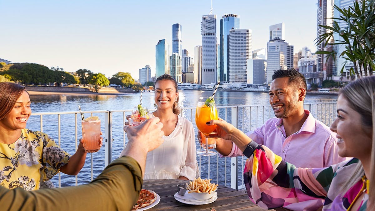 A group of friends alfresco dining and cheering over cocktails at riverside bar brisbane city