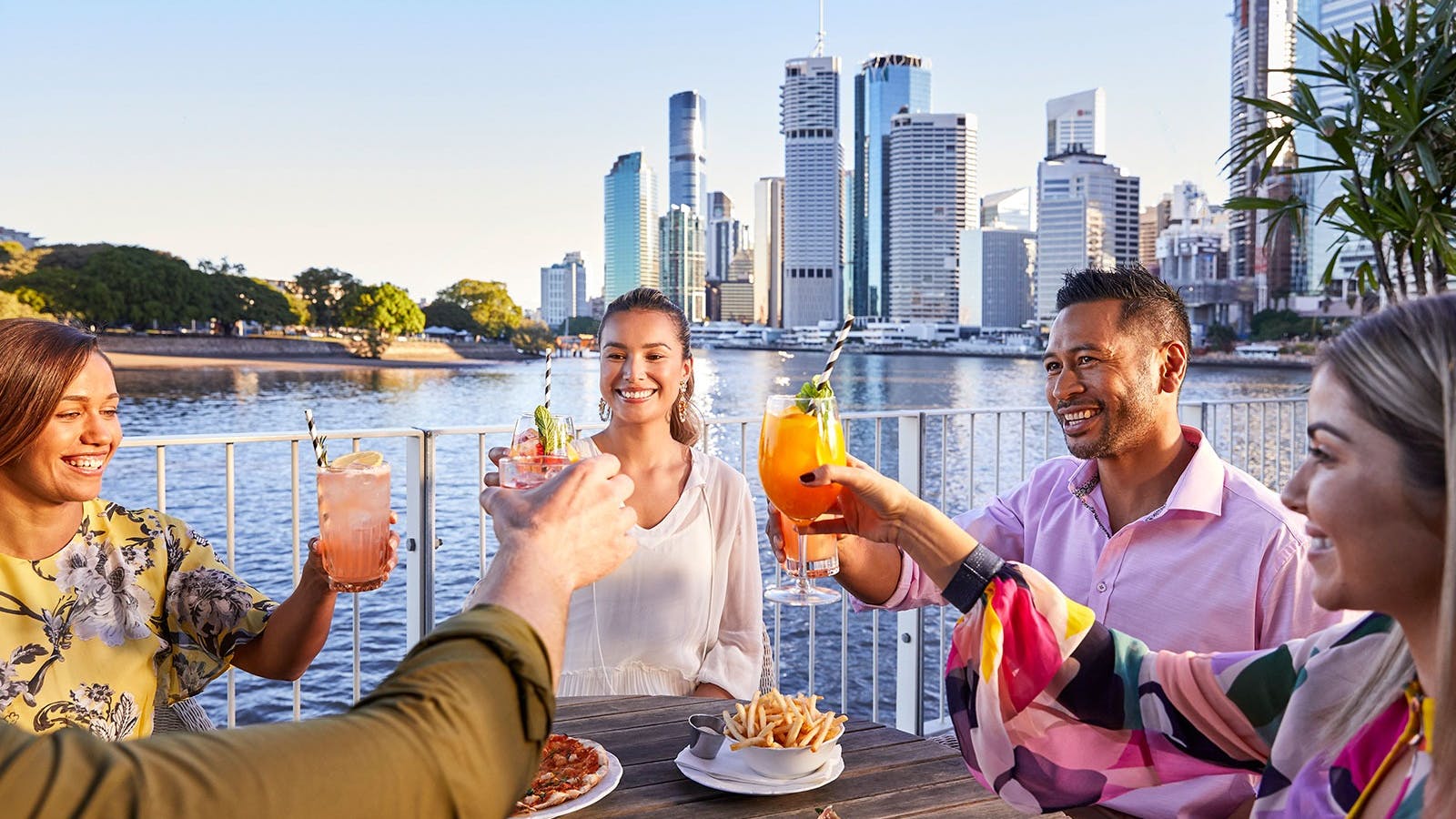 A group of friends alfresco dining and cheering over cocktails at riverside bar brisbane city A group of friends alfresco dining and cheering over cocktails at riverside bar brisbane city